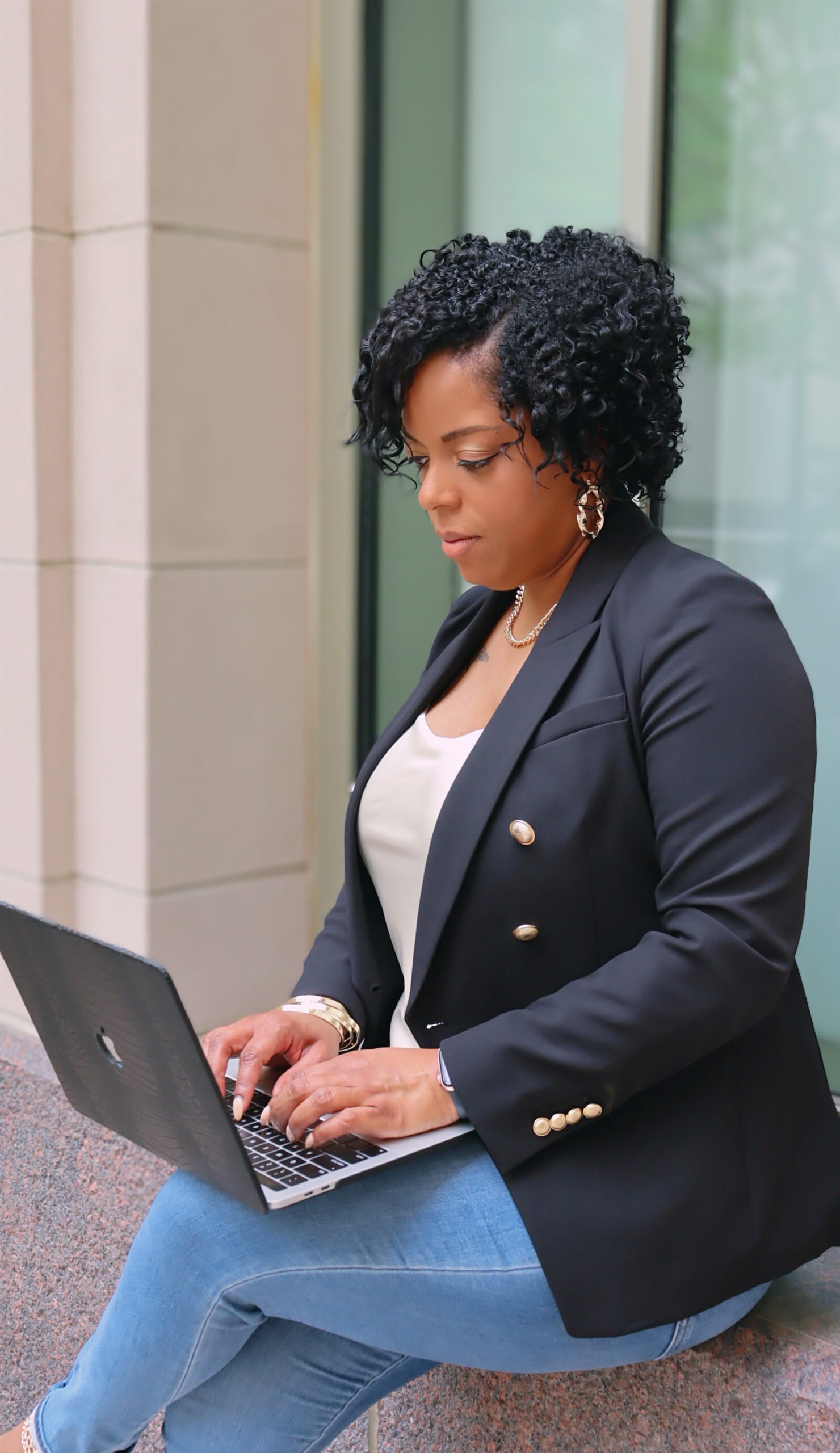 African American Woman solopreneur sitting in window typing on laptop