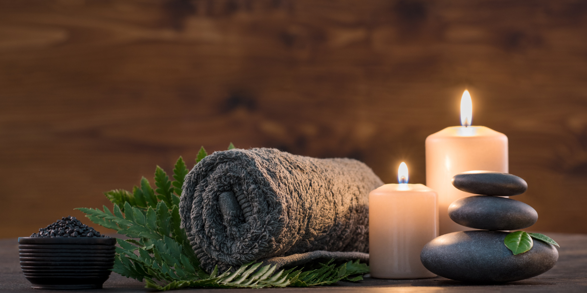 Spa Treatment for self-care, brown towel on green fern with candles and black stones